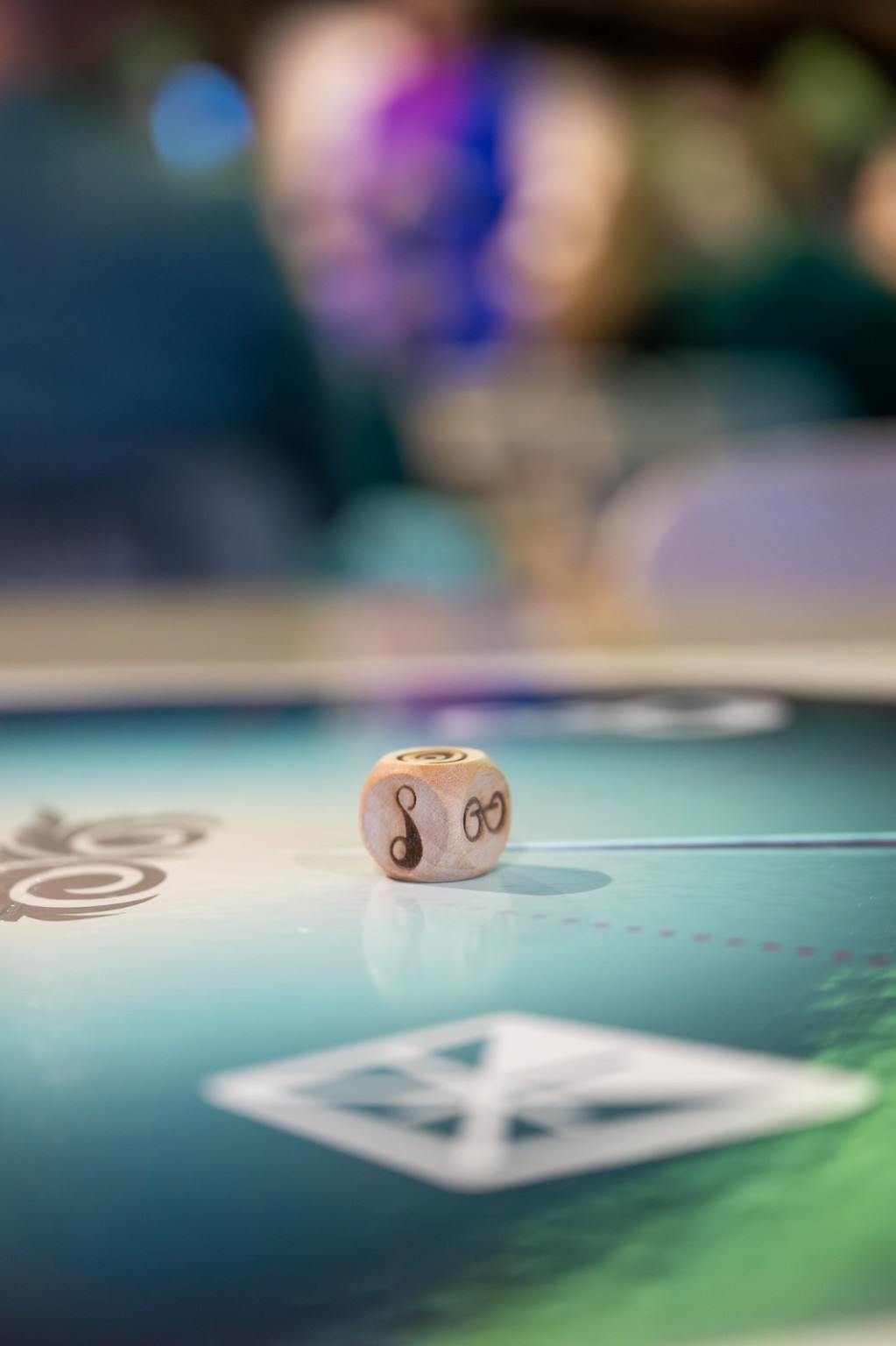 Dobbelsteen op het Intuïst spelbord, met deelnemers op de achtergrond